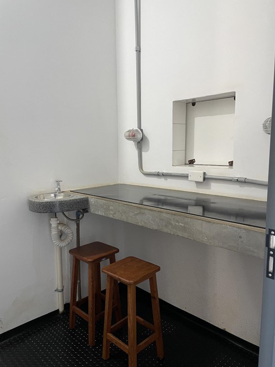 Bancada do Laboratório, contendo uma pia redonda pequena com uma torneira, e dois bancos de madeira em frente à bancada